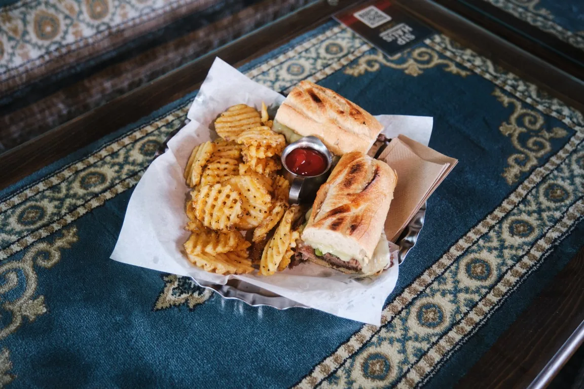 Sip Haus Philly Cheesesteak with waffle fries and ketchup on a Persian rug table